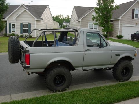 1995 Ford Bronco - This modified Ford Bronco features an external roll cage and a spare tire carrier, seen parked in front of houses.