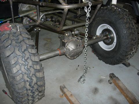 1995 Ford Bronco - The rear axle and suspension components of a custom-built off-road vehicle are shown, large tires and a roll cage.