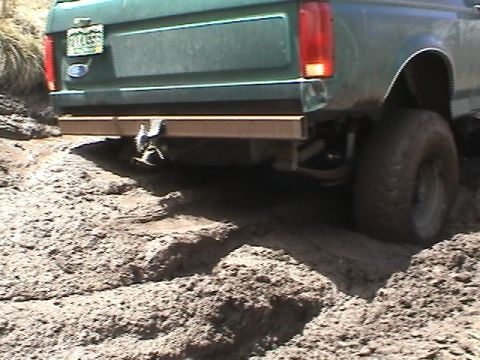 1979 Ford Bronco - This 1979 Ford Bronco navigates a muddy off-road trail, showing its rear end and large tires.