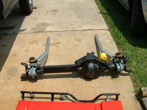 1995 Ford Bronco - A disassembled front axle assembly is laid out on a concrete driveway next to a red creeper.