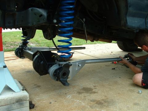 1995 Ford Bronco - A person works on the suspension and axle of a vehicle that is raised on jack stands.
