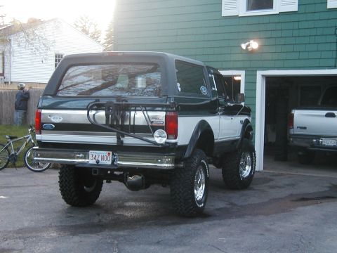 1994 Ford Bronco - This lifted Ford Bronco is parked outside a garage with another truck visible inside.
