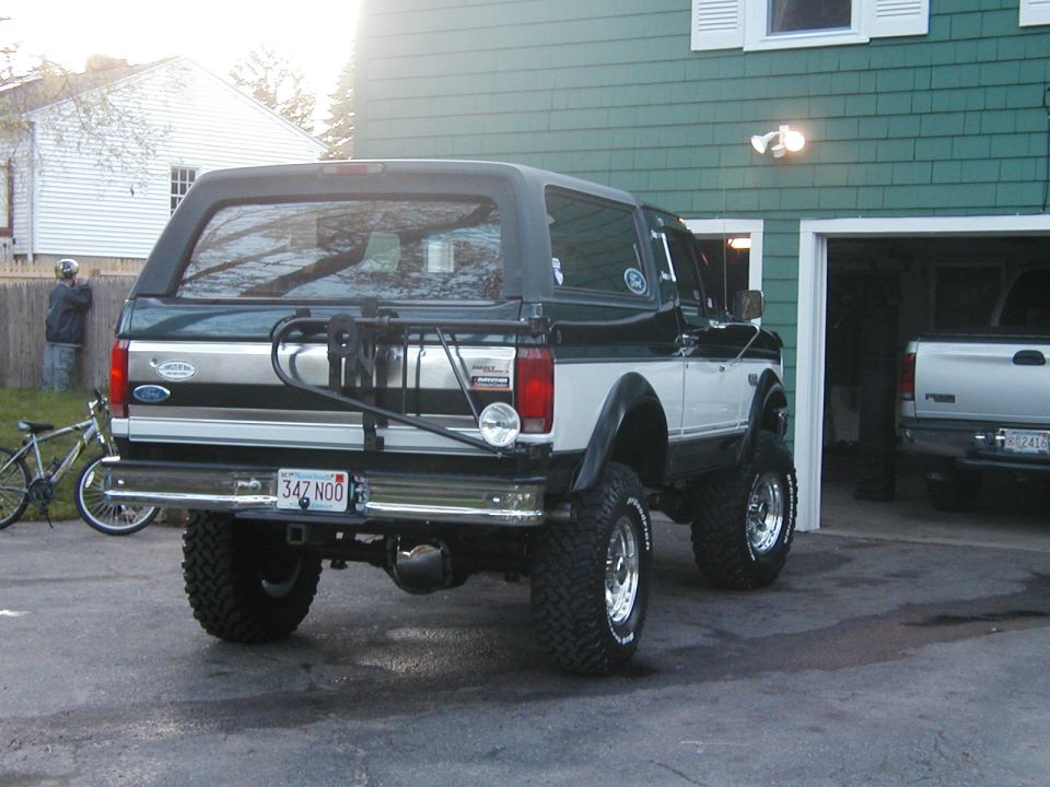 Lifted Ford Bronco with spare tire carrier and bike rack. Another truck is in the garage