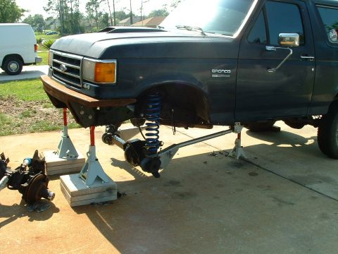 1995 Ford Bronco - A dark blue Ford Bronco is shown with its front end lifted on jack stands, undergoing mechanical work.