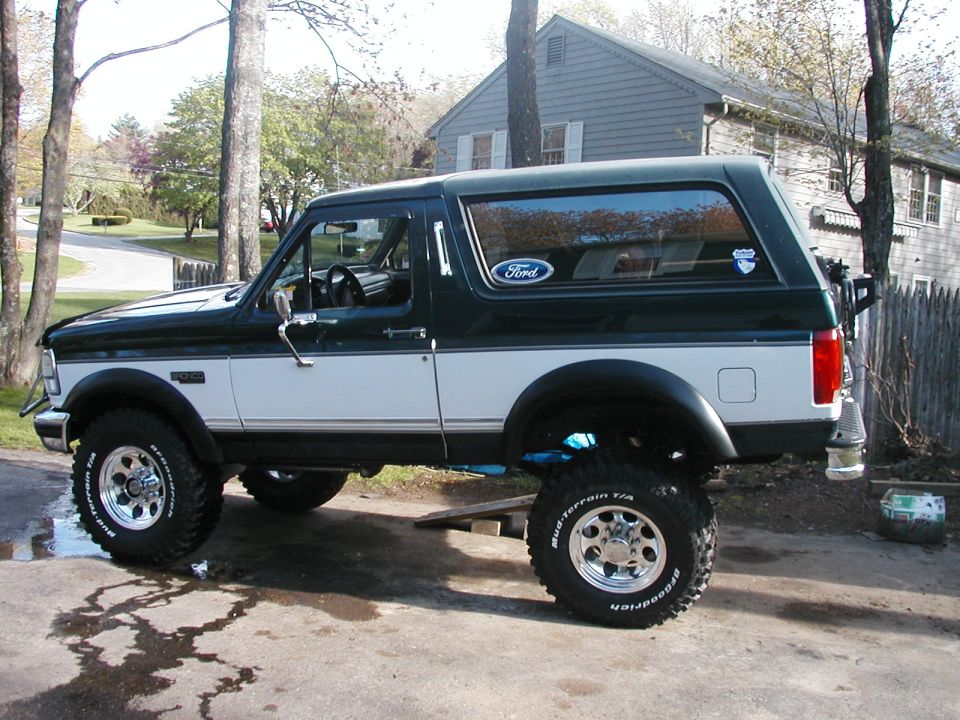 1994 Ford Bronco parked on a driveway, side view. It has a dark green top and white lower body