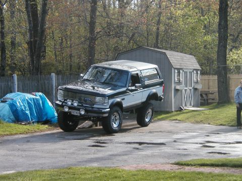 1994 Ford Bronco - A lifted two-tone Ford Bronco is parked in a driveway next to a shed.