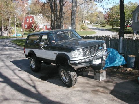 1994 Ford Bronco - A lifted Ford Bronco is parked on concrete blocks in a driveway, with a residential house in the background.