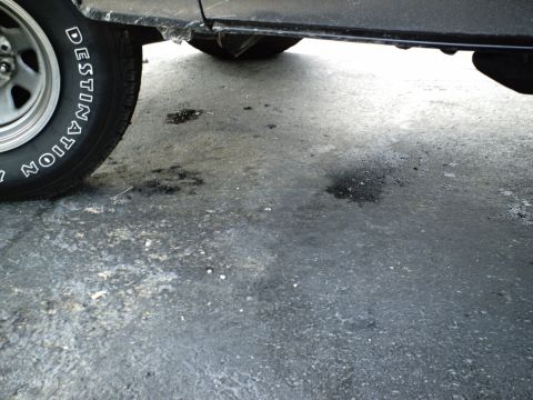 1987 Ford Bronco - Close-up of a vehicle's lower body and tire, showing stains on the ground below.