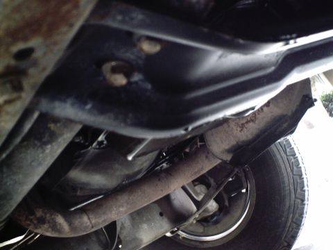 1987 Ford Bronco - A close-up view of the undercarriage of a vehicle, showing the exhaust system and a tire.
