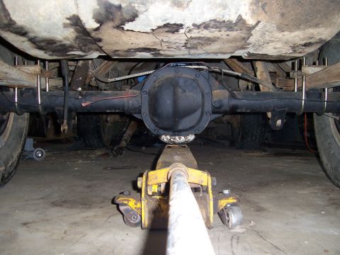 1983 Ford Bronco - Undercarriage view of a vehicle's rear axle and suspension components, with a floor jack providing support.