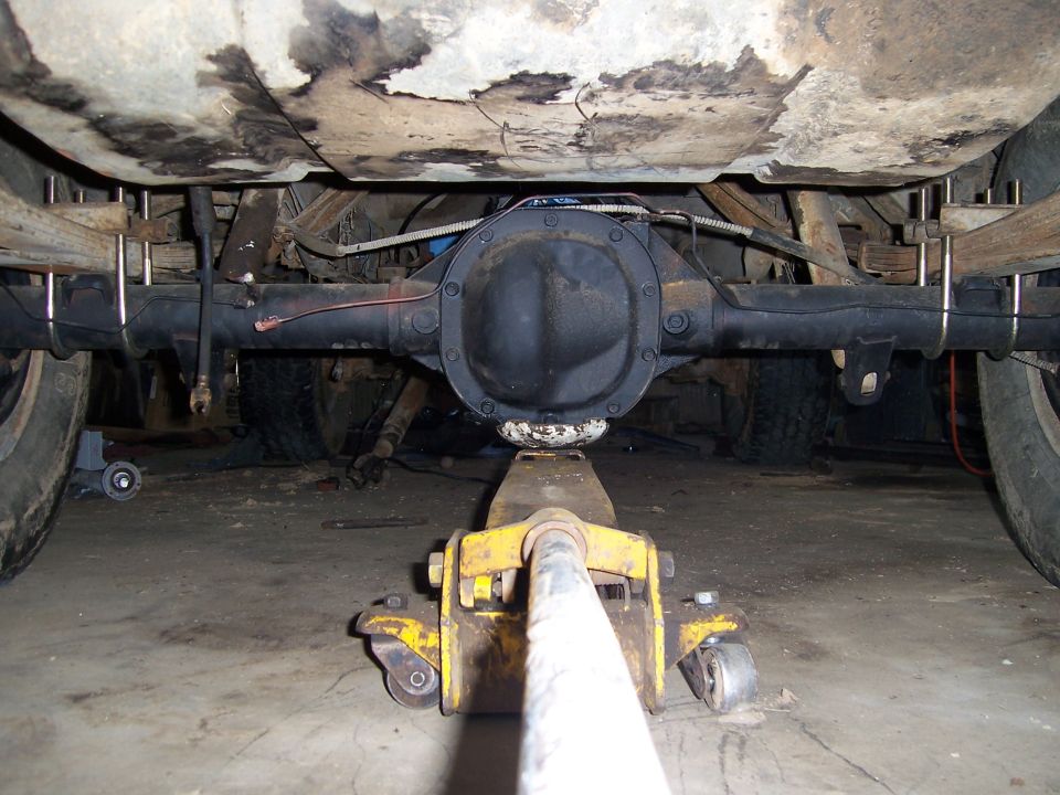 Rear axle assembly supported by a yellow floor jack, with leaf springs and U-bolts visible