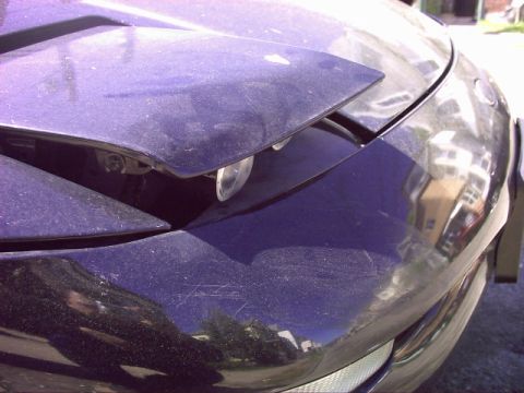 1997 Ford Probe - Close-up of a 1997 Ford Probe's pop-up headlight assembly, showing dust and scratches.