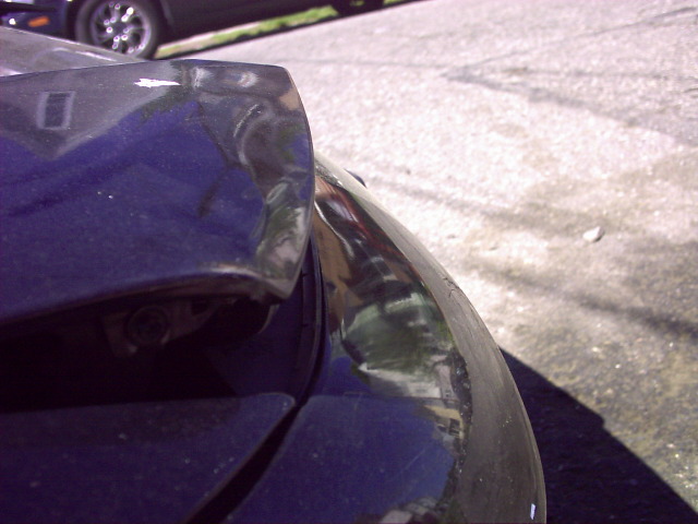 Close-up of a dark-colored car's rear bumper corner with some scuffs and damage