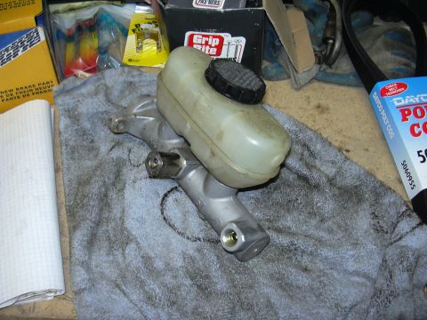 1991 Ford Bronco - A brake master cylinder assembly is shown, likely a replacement part, with various automotive parts and packaging in the background.