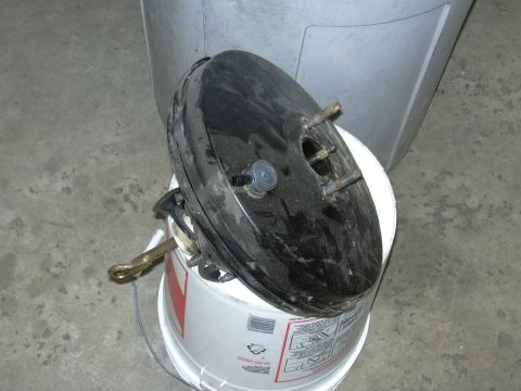 1991 Ford Bronco - A brake booster is shown resting on a bucket, with some text visible on the bucket's label.
