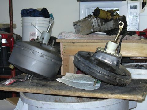 1991 Ford Bronco - Two brake boosters, one silver and one black, are displayed on a workbench with other automotive parts in the background.