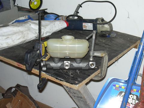 1991 Ford Bronco - A brake master cylinder is clamped to a workbench, with tools and equipment in the background.