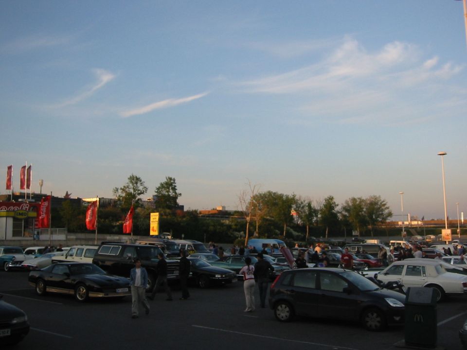 Parking lot scene with many cars and people gathered under a blue sky with wispy clouds