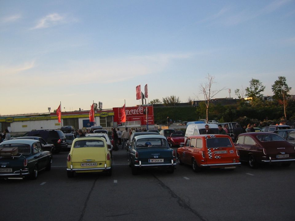 Parking lot scene with several vintage cars, including a yellow car and an orange station wagon, under a blue sky