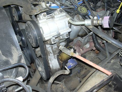 1991 Ford Bronco - Close-up view of engine components, including the air conditioning compressor and associated plumbing.