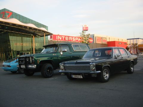 1992 Ford Crown Victoria - A black sedan is parked in front of a commercial building, alongside a green SUV and a blue car.