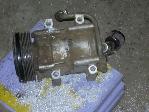 1991 Ford Bronco - Air conditioning compressor with a small filter on a hose, resting on a surface covered in metal shavings.
