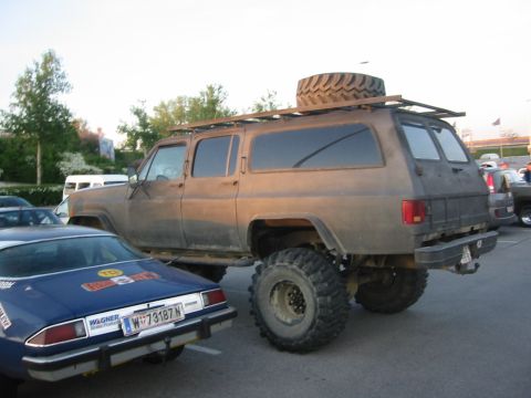 1992 Ford Crown Victoria - A heavily modified SUV with large tires and a roof rack is parked next to a blue car with racing decals.