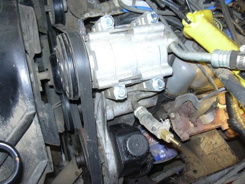 1991 Ford Bronco - Close-up view of the engine bay, focusing on the AC compressor, drive belts, and power steering pump assembly.