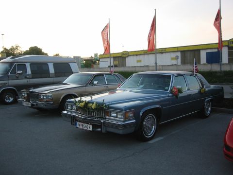 1992 Ford Crown Victoria - Two classic sedans and a van are parked in a lot, with a building and flags in the background.