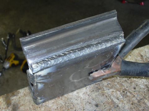 1991 Ford Bronco - Close-up of a welded steel test coupon showing a horizontal weld bead joining two metal pieces, with a copper ground clamp attached at the…