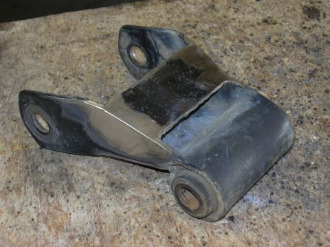 1991 Ford Bronco - A fabricated steel bracket or mount with three bushing/pivot holes and fresh weld and grinding marks, resting on a concrete surface. The me…