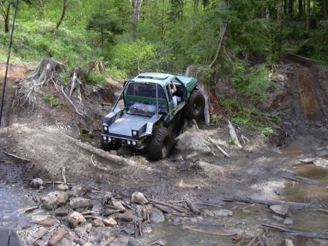 1991 Ford Bronco - A heavily modified off-road vehicle tackles a challenging muddy terrain with steep inclines and obstacles.