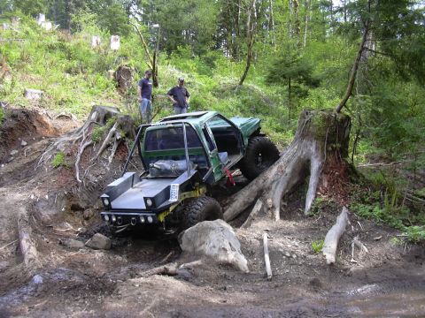 1991 Ford Bronco - Modified off-road vehicle with a roll cage tackles a challenging muddy terrain with large tree roots and stumps.