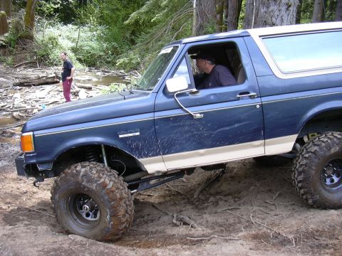 1991 Ford Bronco - This 1991 Ford Bronco is shown off-roading in a wooded area with a stream nearby.