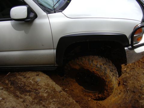 1991 Ford Bronco - White pickup truck's front wheel is deep in mud, stuck off-road.