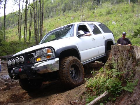 1991 Ford Bronco - A white SUV navigates a steep, muddy incline in a wooded area.