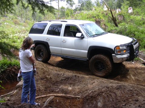 1991 Ford Bronco - A white SUV navigates a muddy, off-road trail with a person pointing in the foreground.