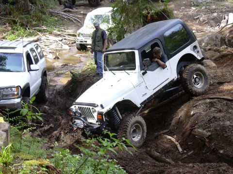 1991 Ford Bronco - A white Jeep Wrangler TJ tackles a challenging off-road course with other vehicles nearby.