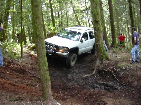 1991 Ford Bronco - A white SUV with off-road modifications is seen driving through a muddy, wooded area.