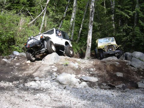 1991 Ford Bronco - Two Jeeps navigate a challenging off-road trail through a wooded area.