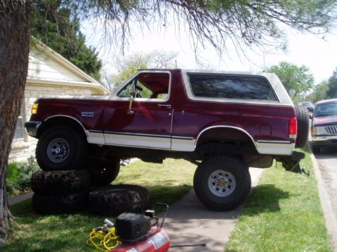 1990 Ford Bronco - This lifted Ford Bronco is parked on tires, possibly for maintenance, with an air compressor and tools visible.