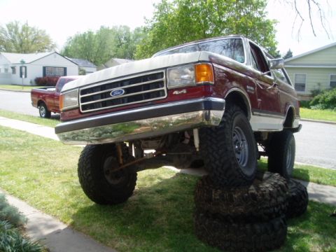 1990 Ford Bronco - A modified Ford Bronco is parked on a stack of tires in a residential area.
