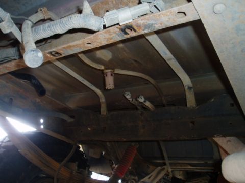 1990 Ford Bronco - Underbody view shows fuel tank, lines, and wiring harness with a rusty frame.