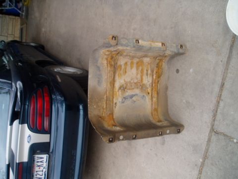 1990 Ford Bronco - A heavily rusted metal component is shown next to the rear of a dark blue vehicle.
