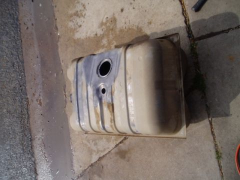 1990 Ford Bronco - A detached metal fuel tank rests on a concrete surface, showing signs of wear and use.