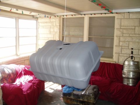 1990 Ford Bronco - A large, gray fuel tank is suspended by a rope, with two couches visible behind it.