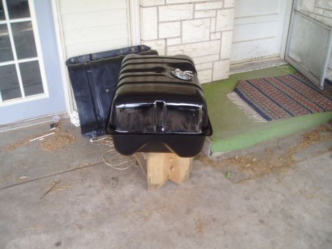 1990 Ford Bronco - A black fuel tank sits on wooden blocks outside a building, with another part behind it.