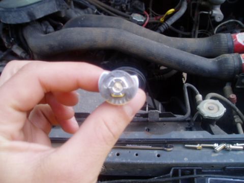 1990 Ford Bronco - A hand holds a bolt in front of an engine bay, with a Supermotors.net logo visible at the bottom.