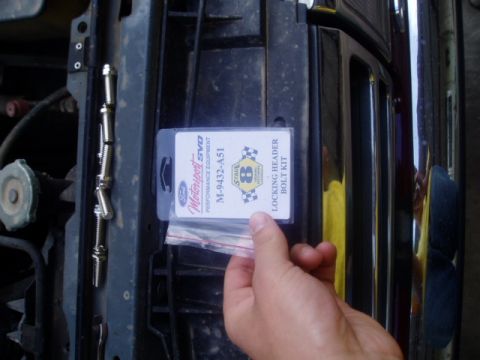 1990 Ford Bronco - A hand holds a Ford Motorsport SVO locking header bolt kit near a vehicle's grille.