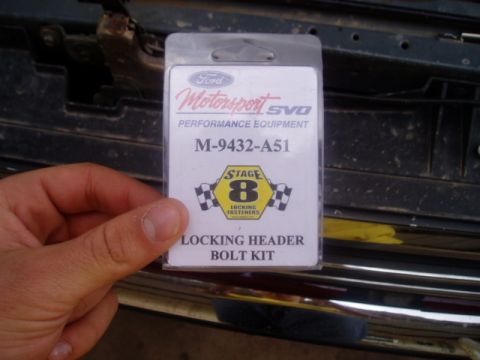 1990 Ford Bronco - A package for a Ford Motorsport SVO locking header bolt kit is held in front of a vehicle's engine bay.